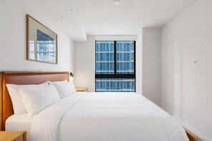 A hotel room with a large bed, a wooden headboard, a nightstand, a framed picture on the wall, and a window with a view of buildings. - The Crosby - 22nd Fl - City Views - Free Spa (Miami)