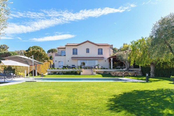 A two-story house with a swimming pool, a covered patio, and a well-maintained lawn.