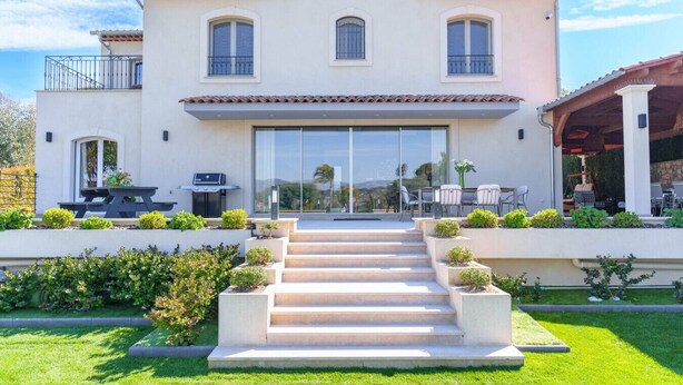 Ein zweistöckiges Haus mit einer Terrasse, einem Grill und einer Treppe, die zum Eingang führt.