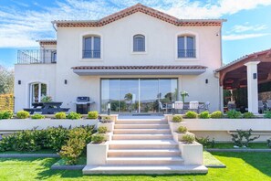 A two-story house with a patio, a barbecue, and a staircase leading to the entrance.