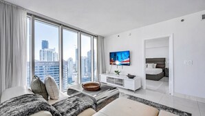 Una habitación de hotel moderna con un ventanal grande, un televisor de pantalla plana, un sofá, una cama y una pequeña zona de comedor.