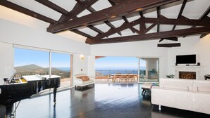 Uma sala de estar espaçosa com um piano, um sofá branco, uma lareira e uma televisão.