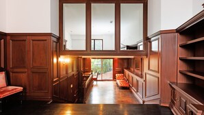 Um corredor amplo com painéis de madeira, um banco estofado em vermelho e vista para o exterior.