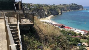 A coastal view with a staircase leading down to a beach, overlooking the sea and a cliff with buildings. - Corallo (Tropea)