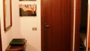 A hallway with a wooden door, a small table with a green tray, and two framed pictures on the wall. - Corallo (Tropea)