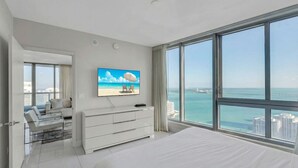 Een moderne slaapkamer met een groot bed, een televisie, een dressoir en uitzicht op de oceaan.