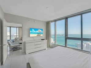Ein modernes Schlafzimmer mit einem großen Bett, einem Fernseher, einem Schminktisch und Meerblick.