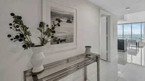 Een modern interieur met een witte console tafel, een lijstwerk schilderij van een landschap, en een uitzicht op een stadsgezicht door grote ramen.