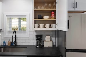 Eine Küche mit Kaffeemaschine, Zucker und Teebehältern, einem Fenster mit Jalousien und einem Kühlschrank.