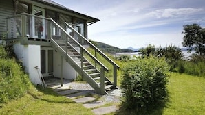 A house with a staircase leading to a porch, surrounded by greenery and a view of a lake. - Tigh na Mara - Sleeps 4, Sea Views & Pet Friendly (Oban)