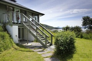 A house with a staircase leading to a porch, surrounded by greenery and a view of a lake. - Tigh na Mara - Sleeps 4, Sea Views & Pet Friendly (Oban)