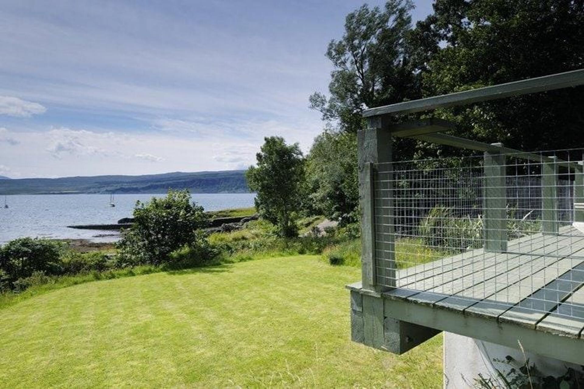 A grassy area with a metal fence and a view of a body of water with boats.