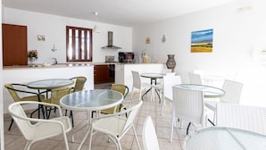 A modern kitchen with white cabinets, a wooden door, and a dining area with white wicker chairs and glass tables. - SALENTINE DAYS - 2 (Torre Lapillo)