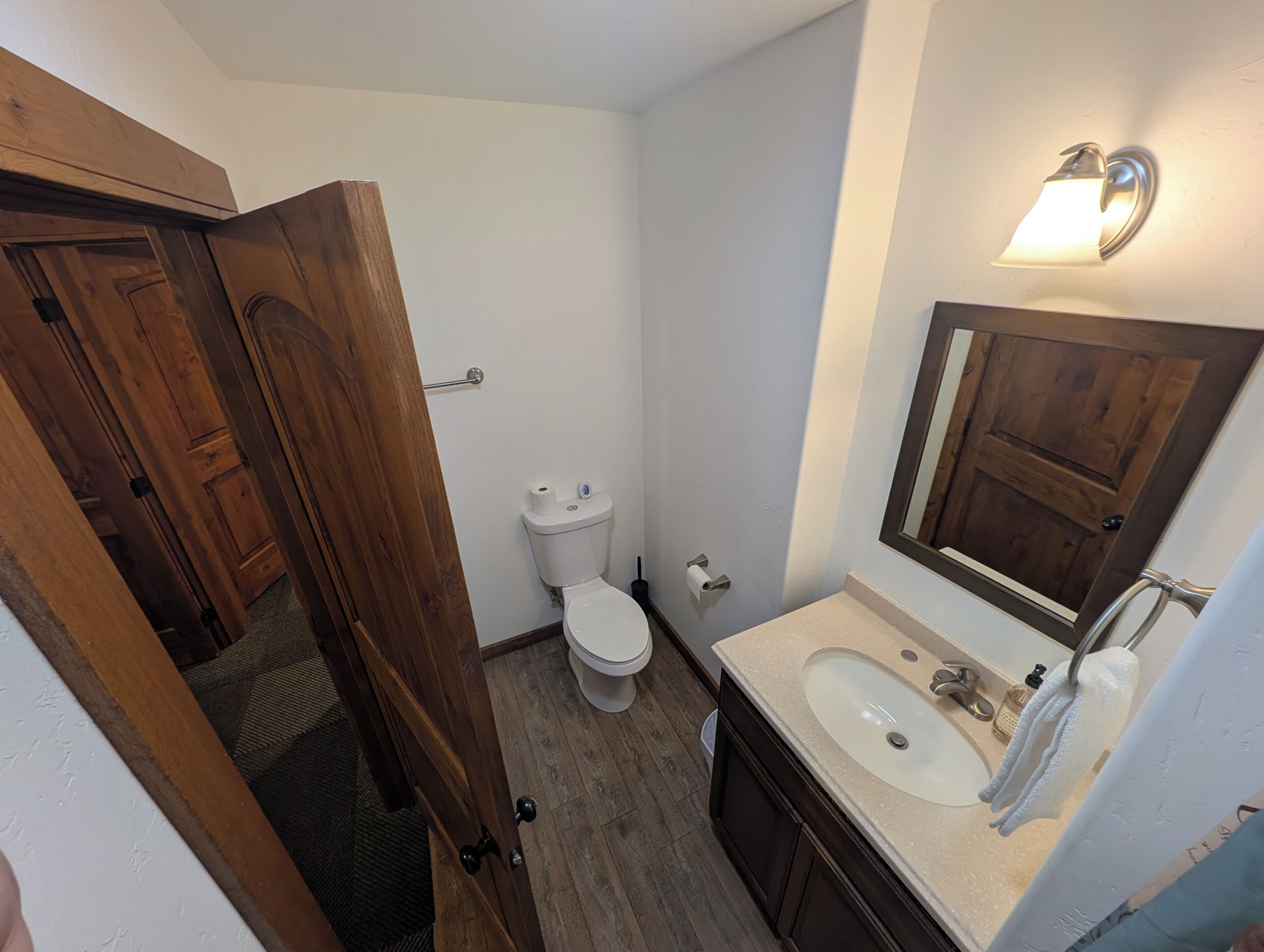 A bathroom with a wooden door, white toilet, and a sink with a mirror.
