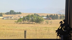 Vista a través de una ventana de un paisaje rural con campos, árboles y colinas distantes.