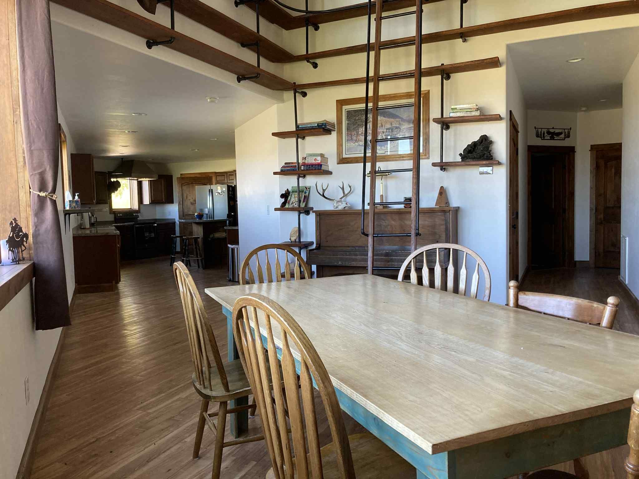 A dining area with a long table, four chairs, and a wooden ceiling with exposed beams.