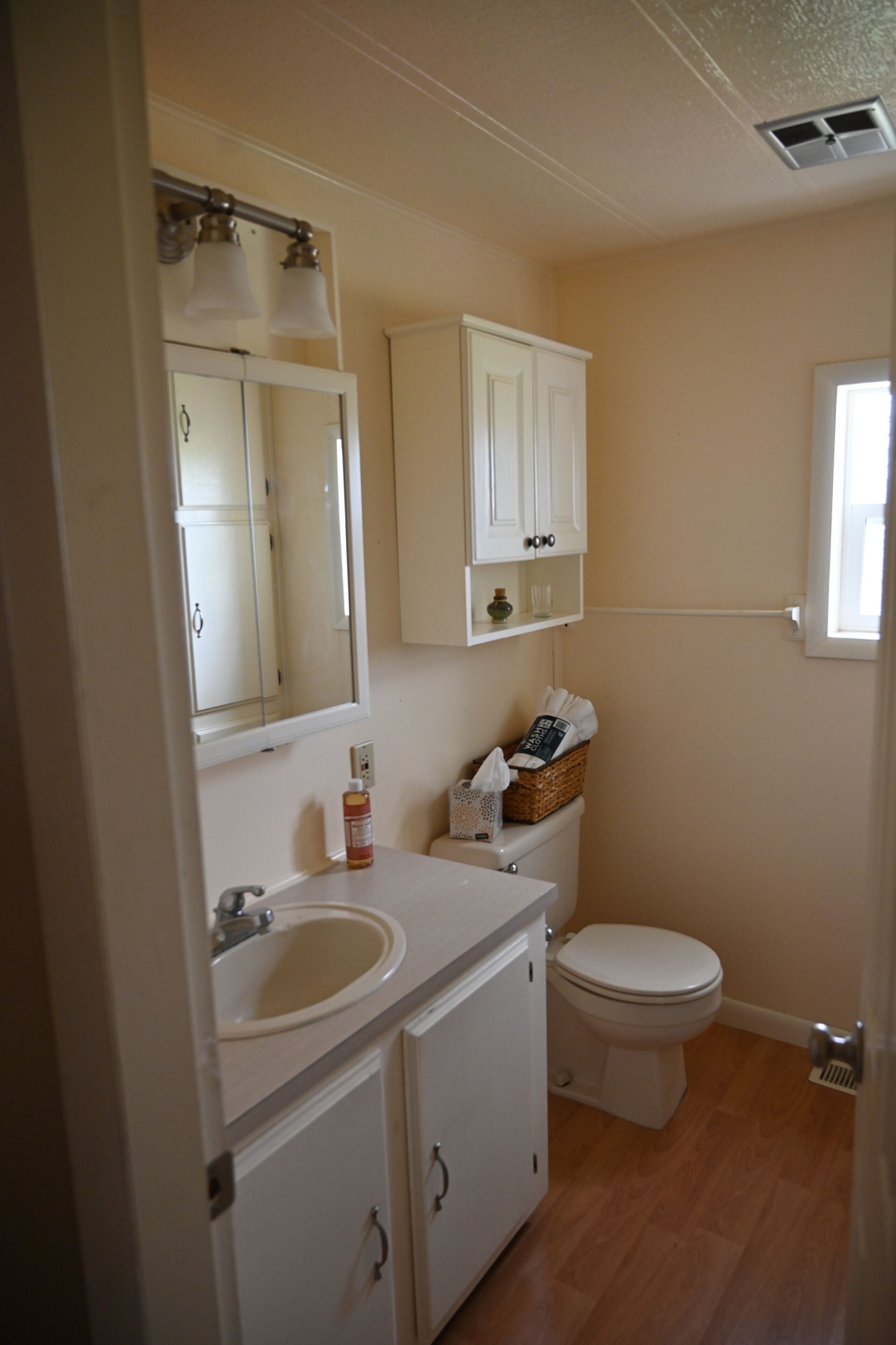 Une salle de bain comprenant un lavabo, un miroir, un meuble de rangement, des toilettes et une fenêtre.