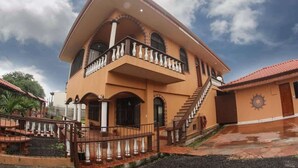 Un edificio a due piani con un balcone, una scala e un emblema solare sulla parete.