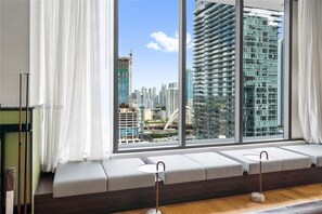 Ein modernes Zimmer mit einem großen Fenster, einer gepolsterten Bank und Blick auf eine Stadtlandschaft.