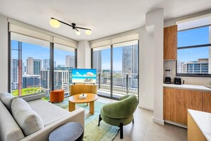 Eine moderne Wohnung mit Balkon, Fernseher, Sofa, grünem Sessel und Küchenzeile.