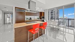 A modern kitchen with a central island, bar stools, and a dining area with a view of the city. - Icon Brickell 2BR Ocean & Pool View + Spa Access (Miami)