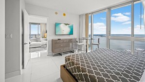 A modern bedroom with a large bed, a TV, a desk, and a view of the sea. - Icon Brickell 2BR Ocean & Pool View + Spa Access (Miami)