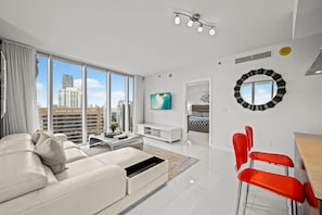 Ein modernes Wohnzimmer mit einem weißen Sofa, roten Sesseln, einem Fernseher und einem großen Fenster mit Blick auf die Stadt.