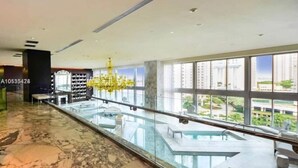 A modern hotel lobby with a glass railing overlooking a pool area, large windows, and a chandelier. - Icon Brickell 2BR Ocean & Pool View + Spa Access (Miami)