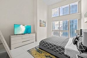 A bedroom with a TV, a bed with patterned bedding, a window with a city view, and a white dresser. - Icon Brickell 2BDR 28th Fl Ocean Views+Spa Access (Miami)