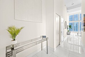 A modern hallway with a glass railing, a potted plant, and a view of high-rise buildings through large windows. - Icon Brickell 2BDR 28th Fl Ocean Views+Spa Access (Miami)