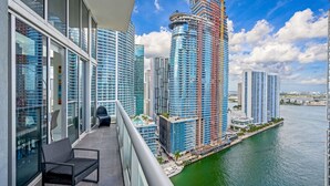 A high-rise building with a construction crane, a balcony with a chair and table, and a river in the background. - Icon Brickell 2BDR 28th Fl Ocean Views+Spa Access (Miami)