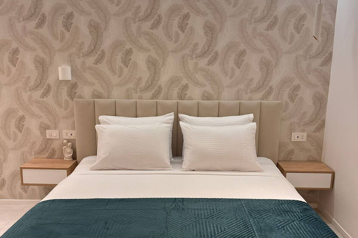 Una cama con un edredón color turquesa, un cabecero con diseño de hojas y dos mesitas de noche con lámparas.