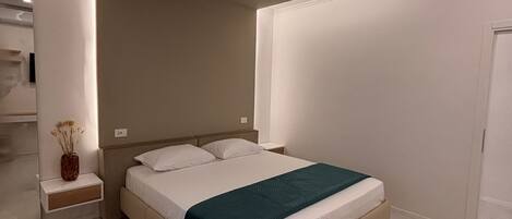 Une chambre à coucher moderne, comprenant un lit, des tables de chevet, une petite table et un vase décoratif.