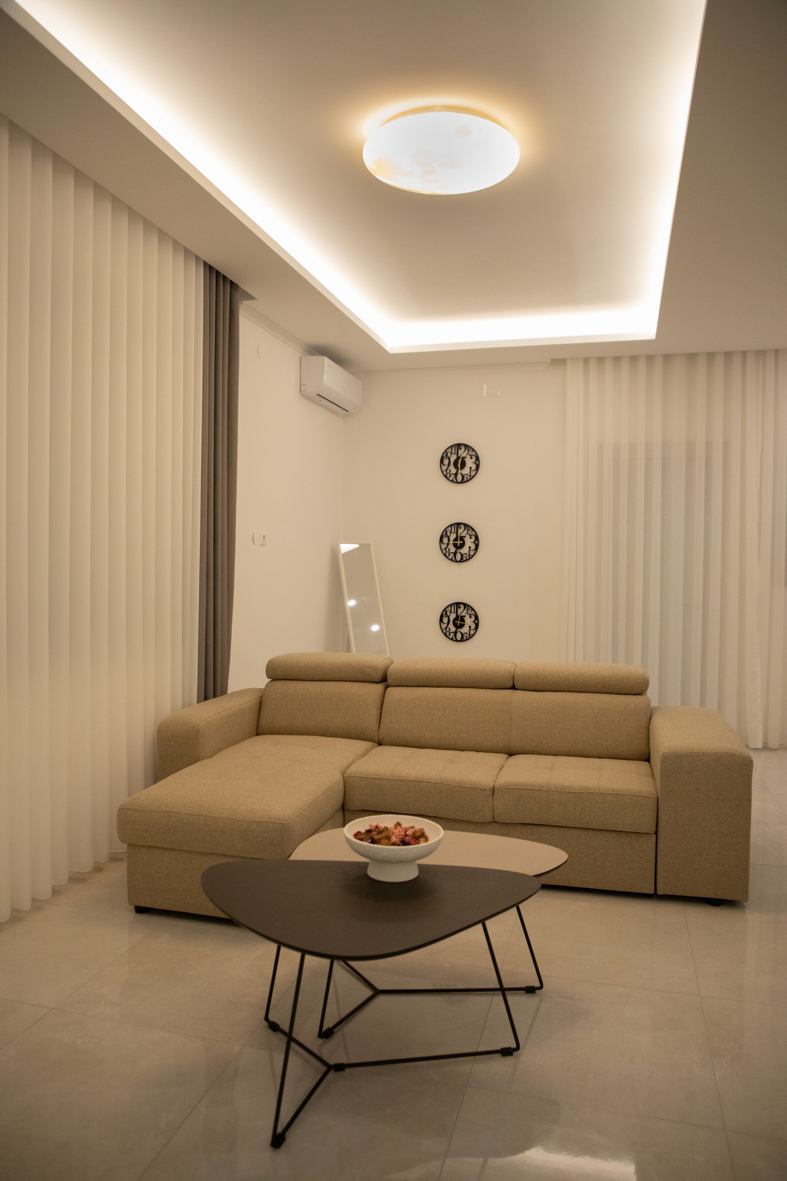 Un salon moderne avec un canapé d’angle, une table basse ronde et trois horloges murales.