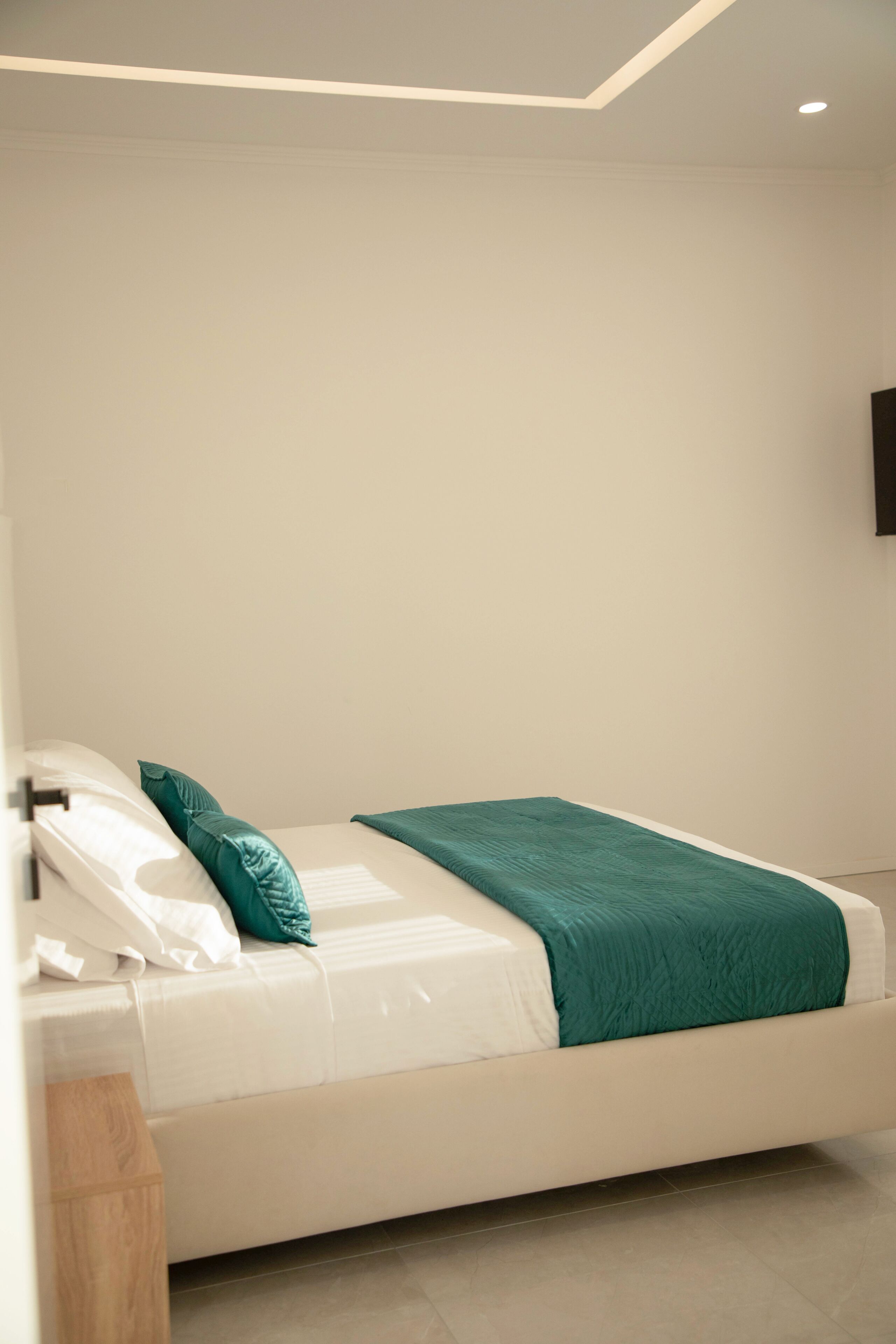 A modern bedroom with a bed, white bedding, a teal throw blanket, and a wooden nightstand.