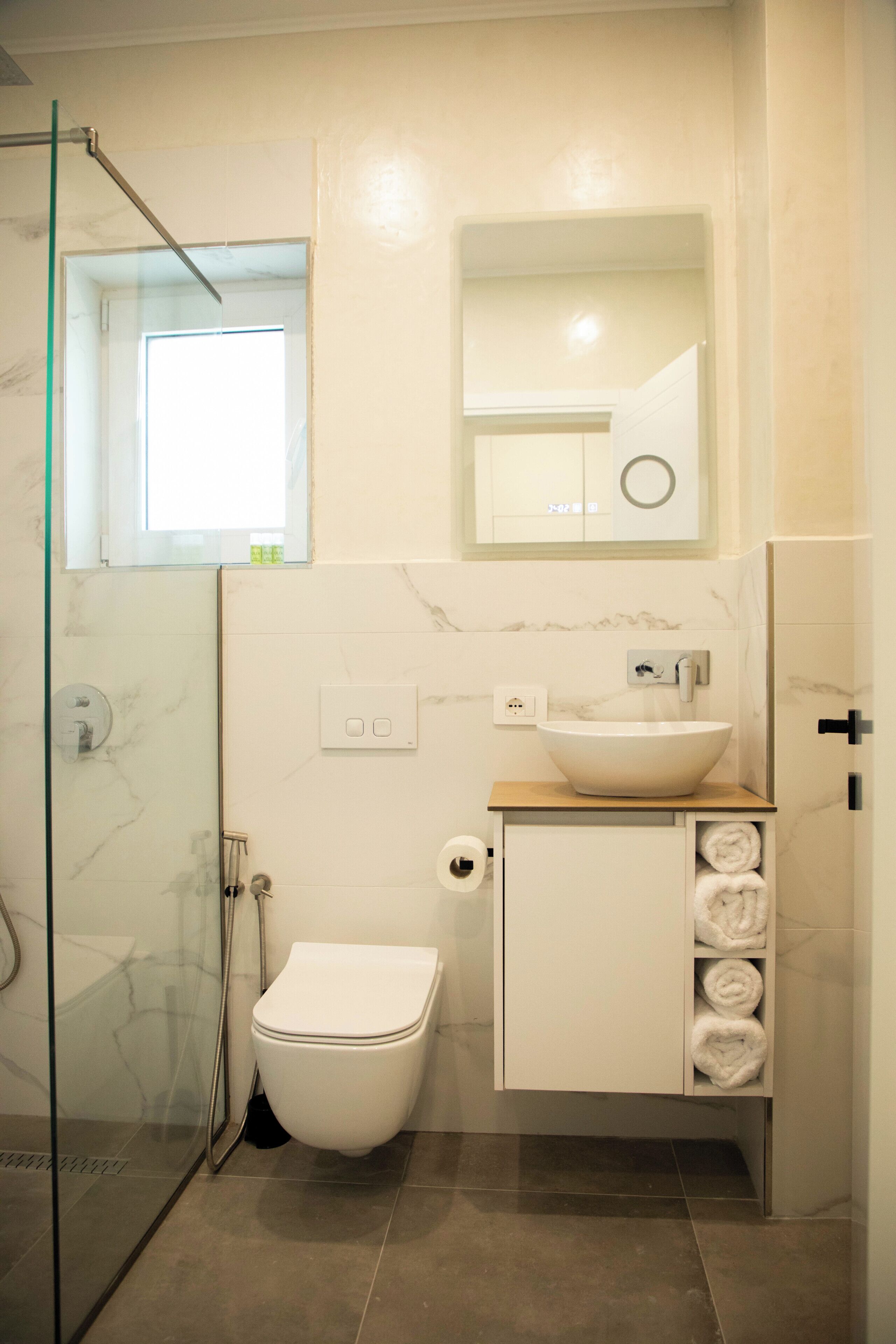 Ein modernes Badezimmer mit Duschkabine aus Glas, einer weißen Toilette, einem Waschtisch und einem Spiegel darüber.