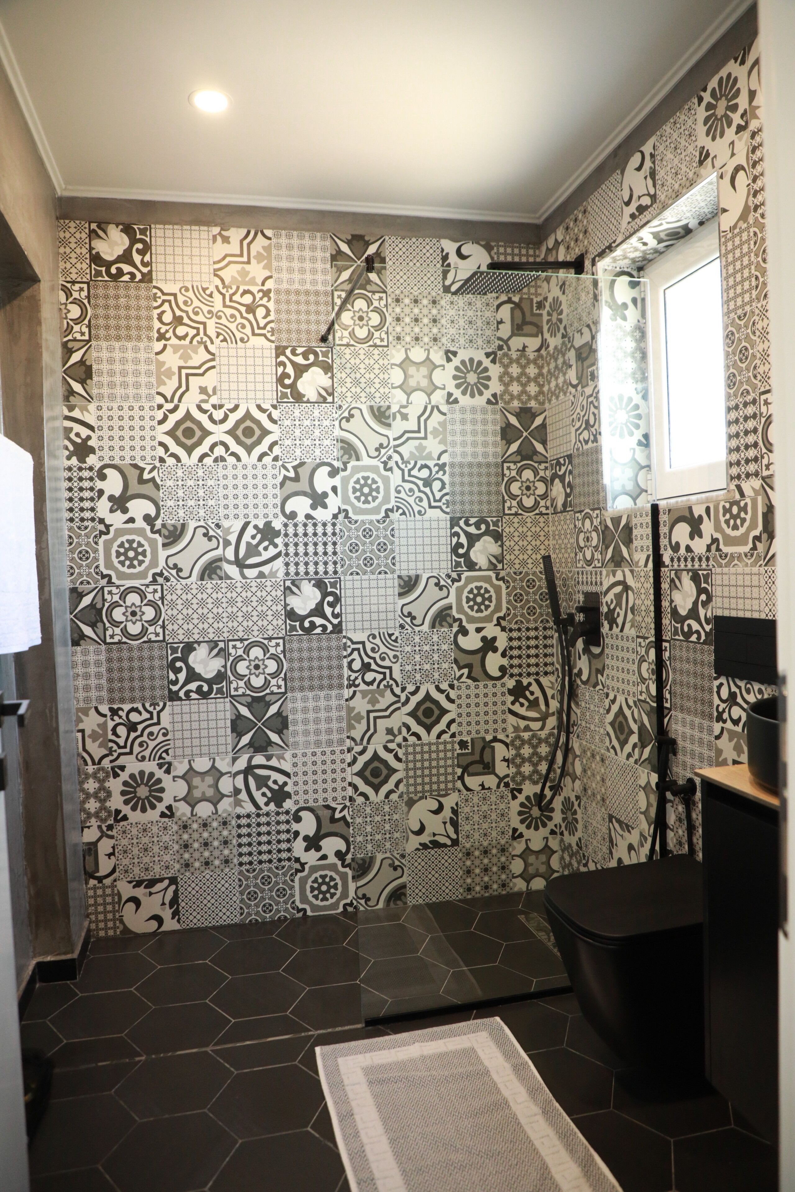 A bathroom with patterned tiles, a shower, a toilet, and a window.