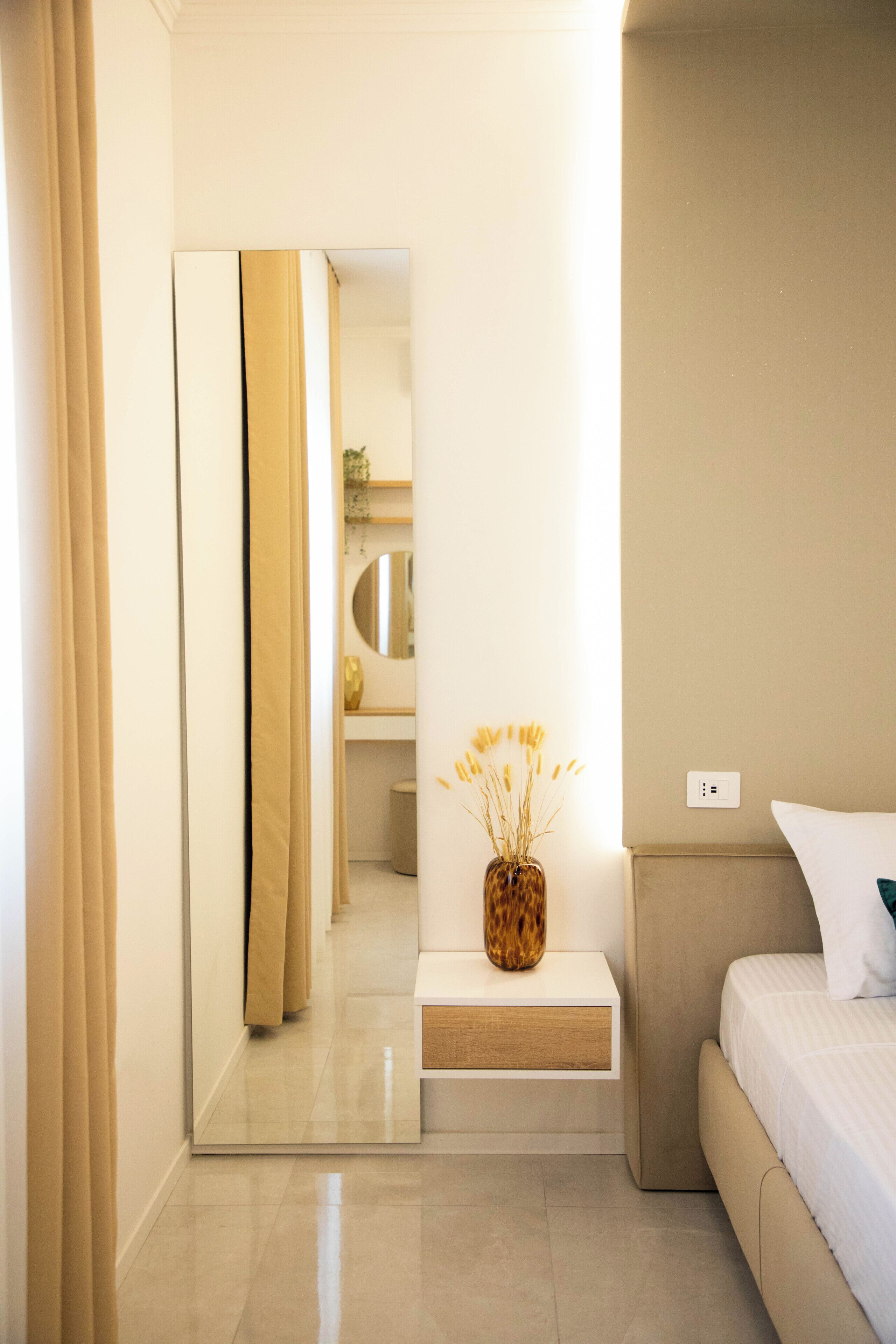 A modern bedroom with a bed, bedside table, and a mirror.