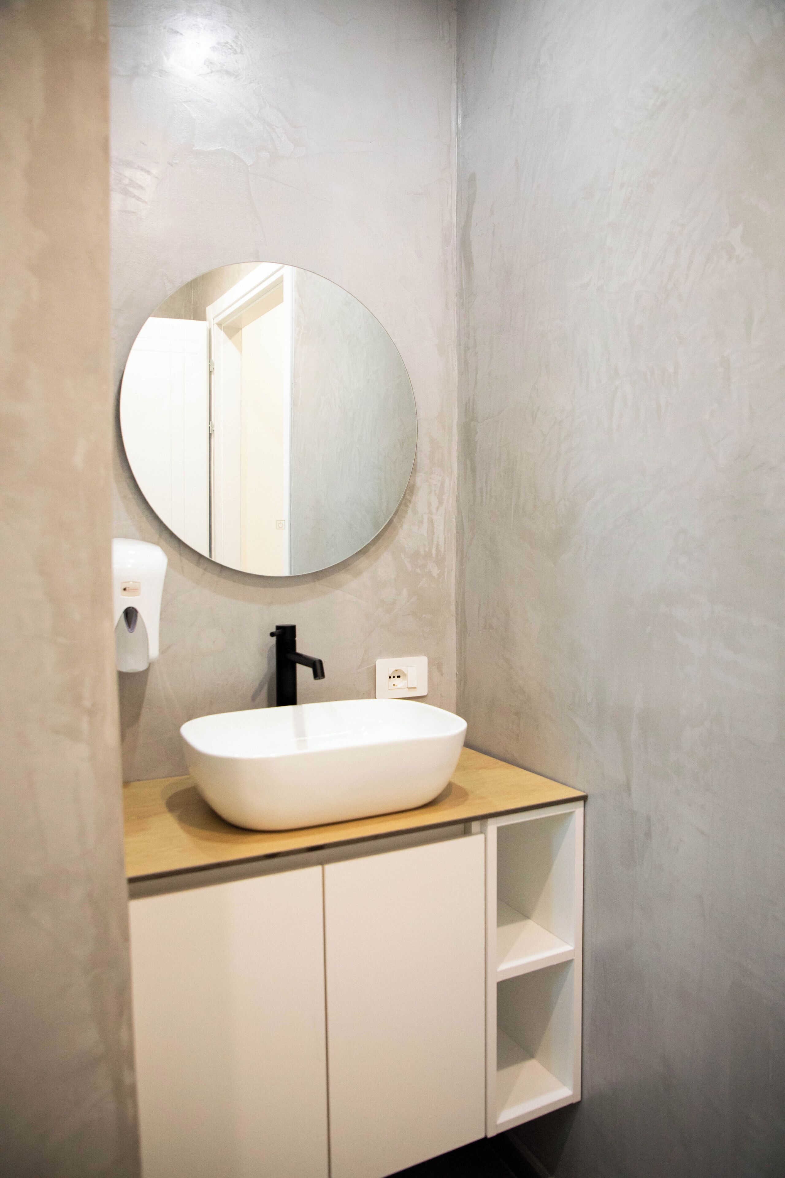 A bathroom with a round mirror, a white sink, and a soap dispenser.
