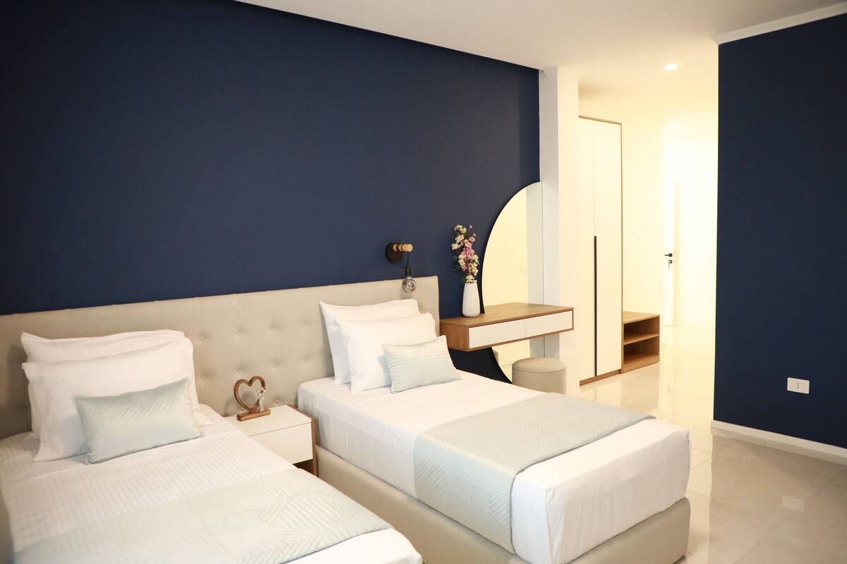 Habitación de hotel con dos camas, una mesita de noche, un espejo y un escritorio pequeño con una silla.
