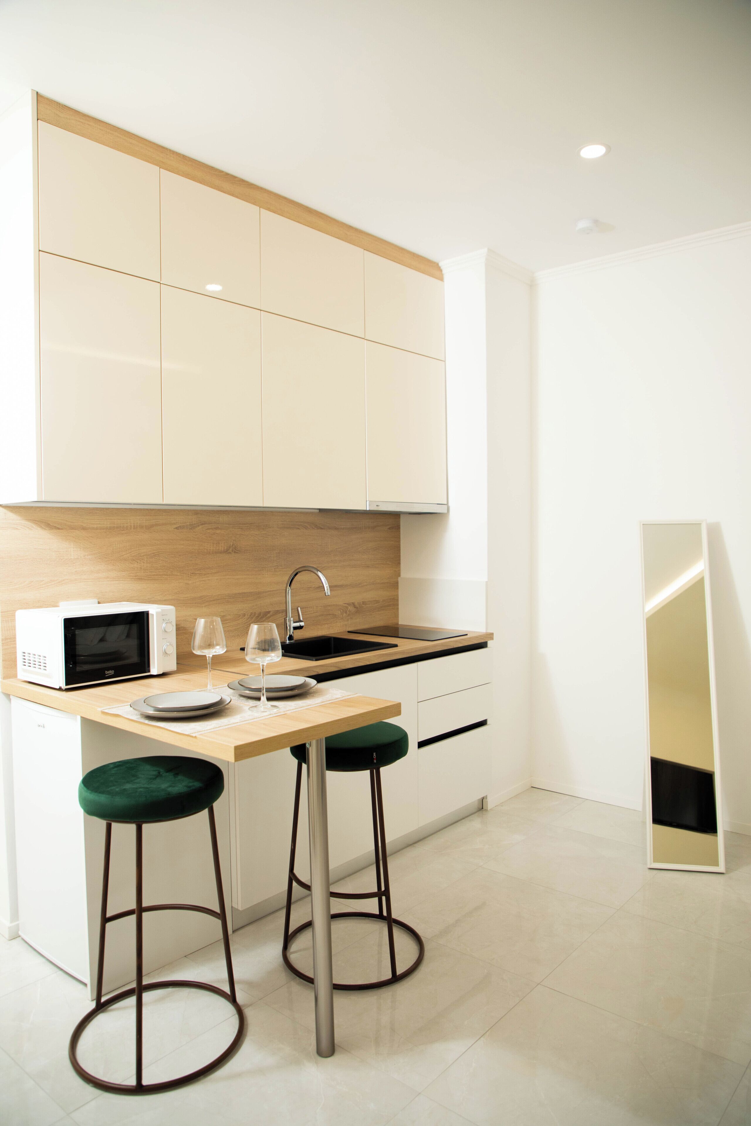 Een moderne keuken met een magnetron, twee krukken, een spoelbak en een spiegel.