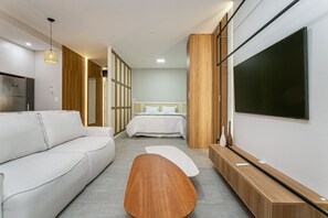 Ein modernes Hotelzimmer mit einer Couch, einem Holztisch, einem Fernseher und einem Bett mit weißer Bettwäsche.