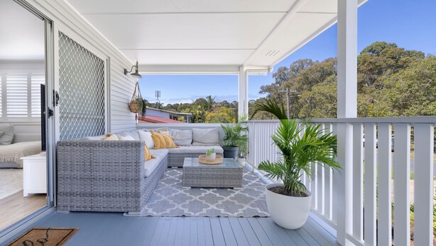 Eine überdachte Veranda mit Gartenmöbeln, einem Blumentopf und Blick auf Bäume und Hügel.