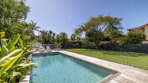 Ein rechteckiger Pool mit Holzterrasse, umgeben von üppiger Vegetation und einem eingezäunten Garten.
