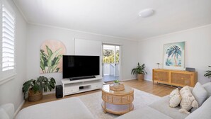 Ein Wohnzimmer mit Flachbildfernseher, einem Rattanschreibtisch, einer Couch, einer Holzkonsole und einem Gemälde.