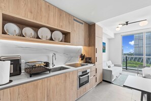 A modern kitchen with wooden cabinets, a built-in oven, a coffee machine, and a large window offering a city view. - City View Studio in Downtown Miami Near Shopping (Miami)