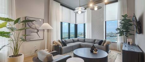 Ein modernes Wohnzimmer mit Ecksofa, rundem Couchtisch und großen Fenstern mit Blick auf die Stadt.