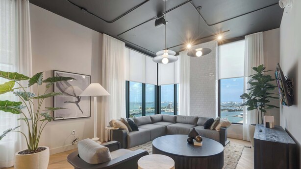 A modern living room with a sectional sofa, round coffee table, and large windows offering a view of the city. - Downtown Miami Condo | Pool / Gym | 2BR (Miami)