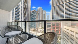 A balcony with wicker chairs and a glass table, overlooking high-rise buildings. - Downtown Miami Condo | Pool / Gym | 2BR (Miami)