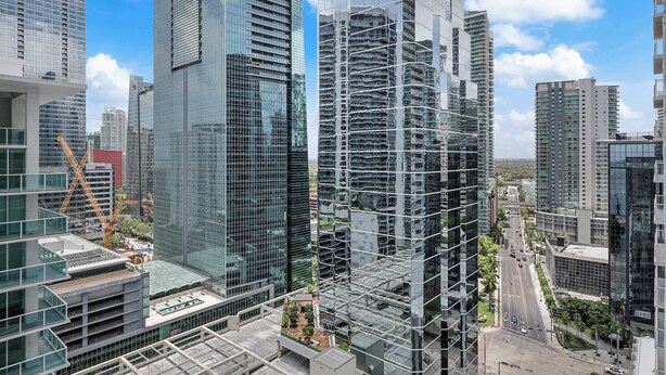 En høj bygning med en moderne glasfacade, omgivet af andre høje bygninger og byggekraner.